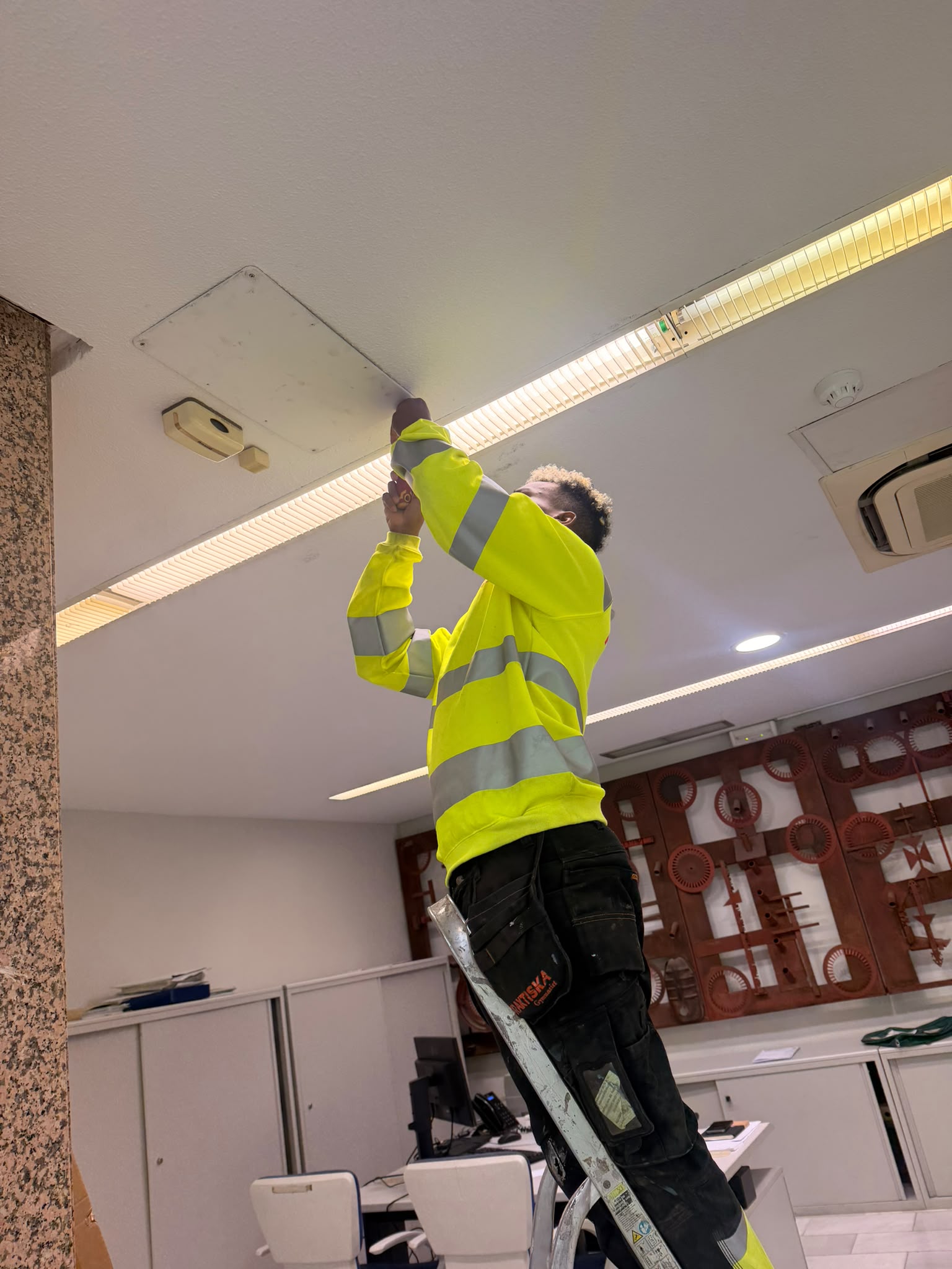 Swedish electrical trainee fitting equipment at ceiling height in an office, one of our Erasmus VET placements in Córdoba